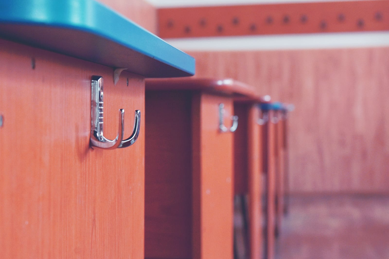 Empty metal coat hooks along a row of school cubbies, the nearest one in focus